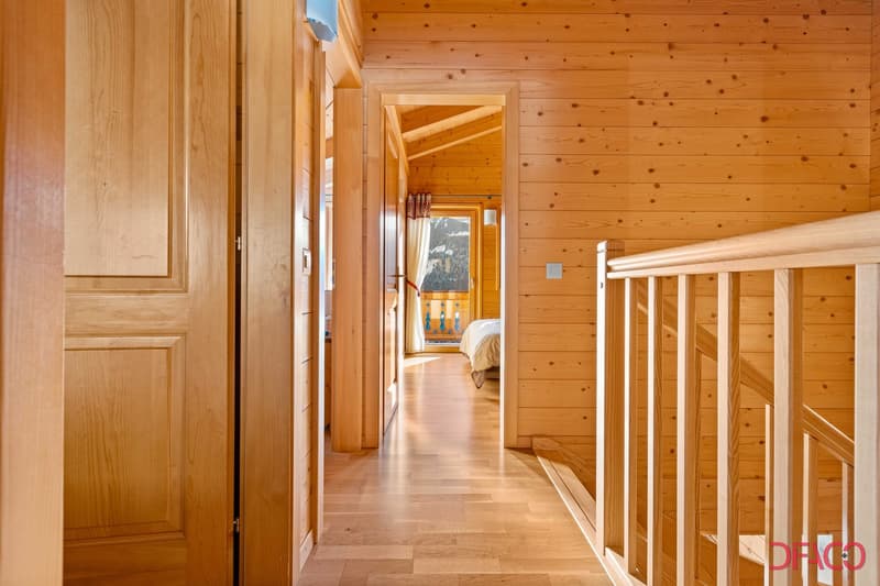 Wooden cabin-style interior with wooden walls and floors, a wooden staircase, and a view of a balcony or terrace through an open doorway.