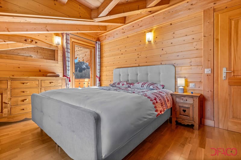 Spacious bedroom with wooden walls and ceiling, large bed with gray headboard, wooden nightstands, and a fireplace visible in the room.