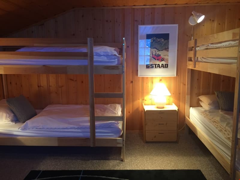 Cozy wooden cabin bedroom with bunk beds, a framed poster on the wall, and a bedside table with a lamp.