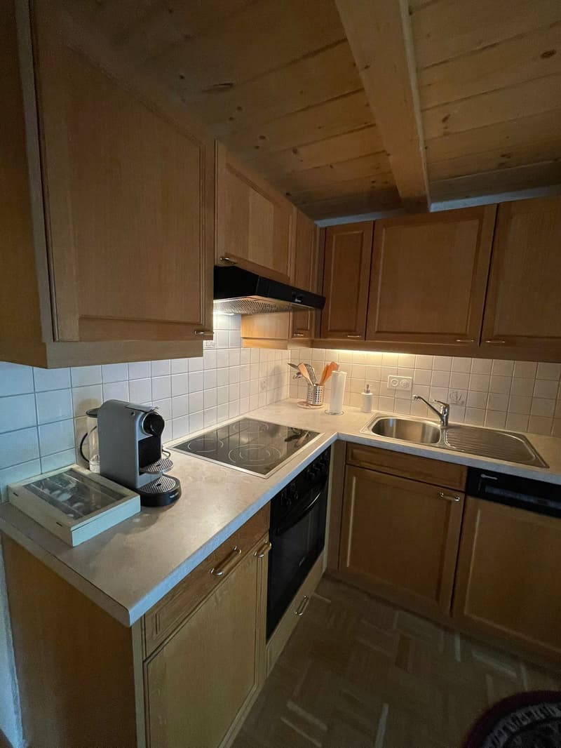The image shows a kitchen with wooden cabinets, a tile backsplash, a sink, a stove, and a dishwasher. The kitchen appears to be in a residential setting.