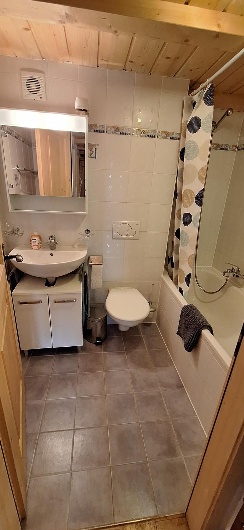 Bathroom with white tiles, vanity sink, toilet, and shower curtain. There is a ventilation fan and a private washing machine visible.