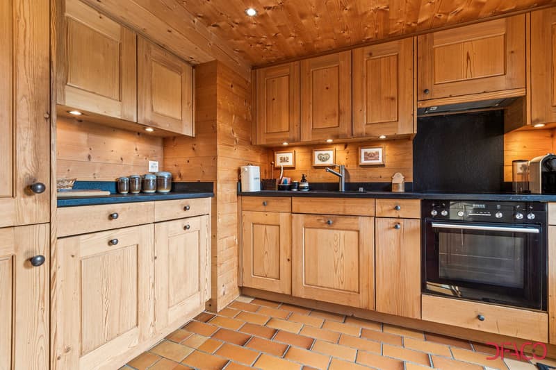 Rustic wooden kitchen with pine paneled walls and ceiling, wooden cabinets, black countertops, and a dishwasher visible.