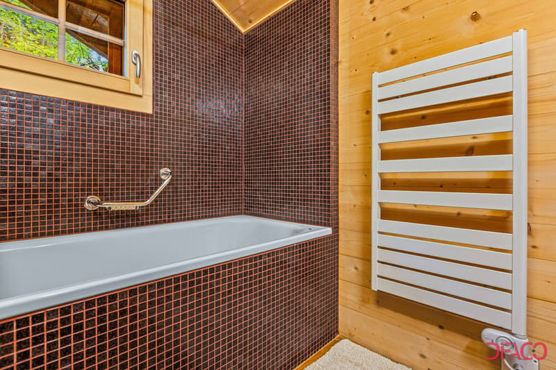 Bathroom with brown mosaic tile walls, a gray bathtub, and a white towel warmer rack.