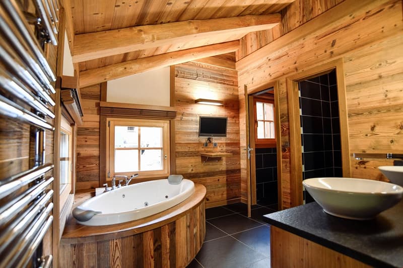 Rustic bathroom with wooden walls and ceiling, large bathtub, TV mounted on the wall, and a black tile floor