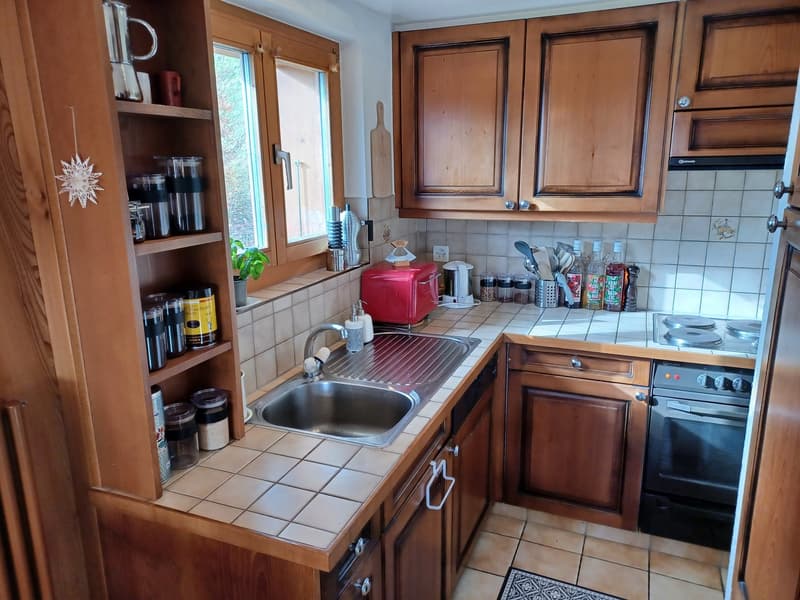 Wooden cabinets, tile countertops, sink, stove, small appliances, shelving with spices and other kitchen items