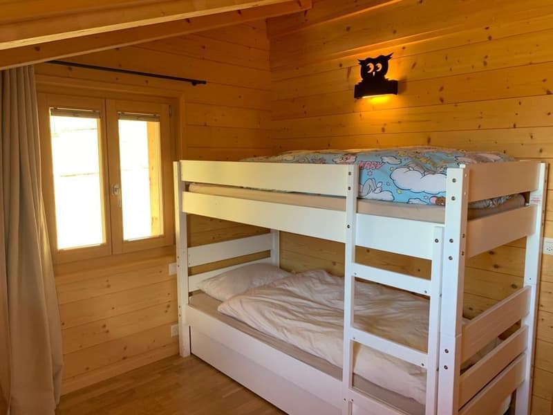 Wooden cabin-style bedroom with bunk beds, wooden walls and ceiling, and a small window.