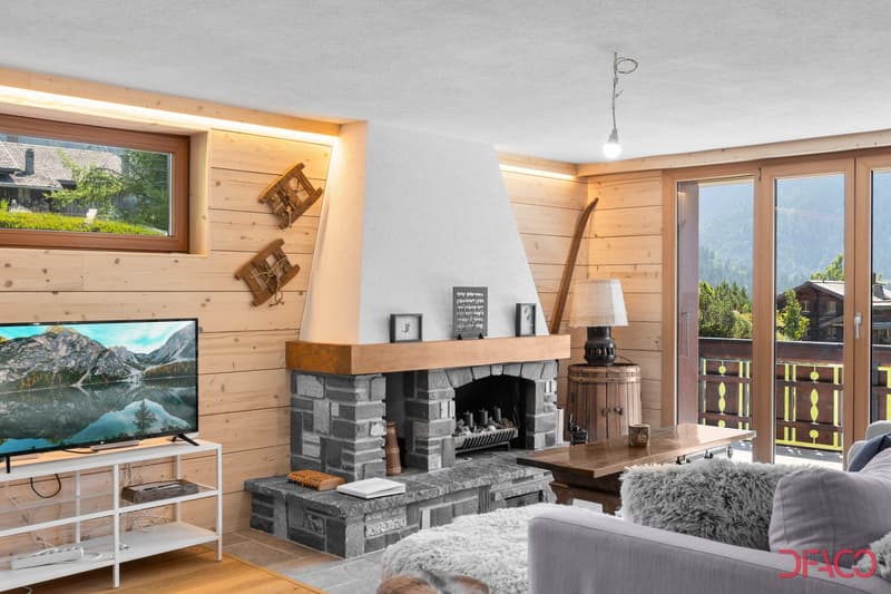 wooden paneled walls, gray stone fireplace, flat screen TV, gray sofa with footrest, wooden coffee table, decorative objects, lamps