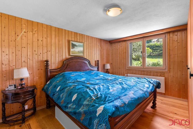 wooden walls, hardwood floor, bed with blue cover, night lamp, nightstand with lamp, framed picture, white window with double doors, white radiator