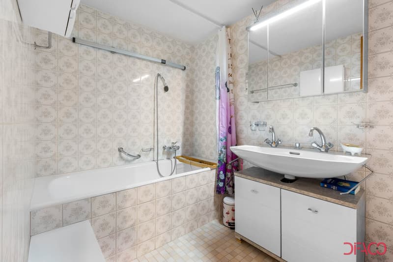 Bathroom with bathtub, sink, tiled walls, and a mirror. Also includes a towel bar and cabinet under the sink. A water heater is attached to the wall.