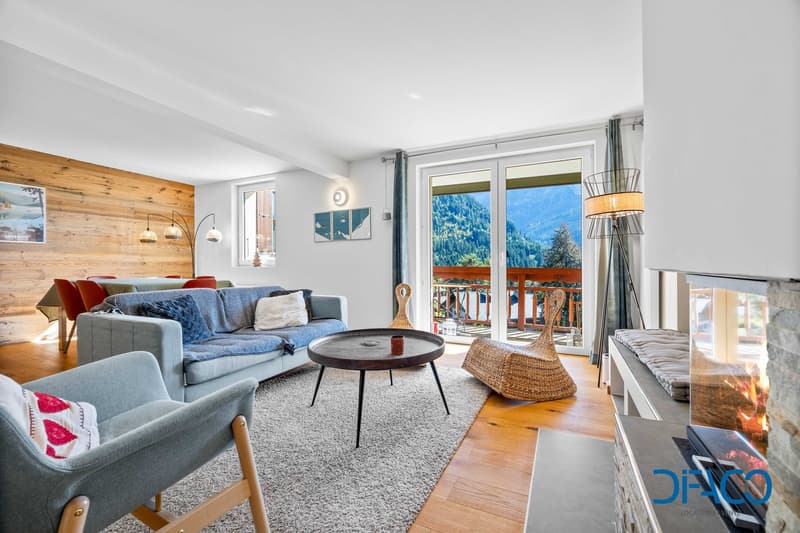 wooden wall, wooden floor, large windows, couch, coffee table, armchair, fireplace, balcony