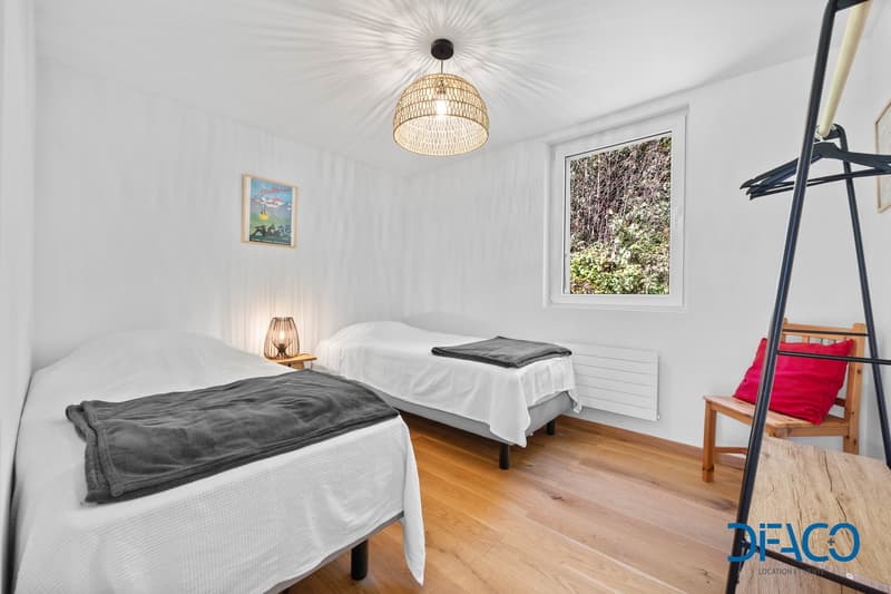 two single beds, a window, a radiator, a wooden lampshade, a framed picture, a wooden chair with a pillow, and a wooden coat rack