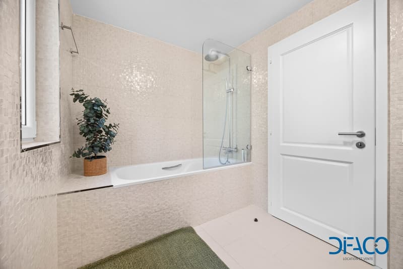 Bathroom: white tiles, bathtub, shower with glass door, green rug, plant