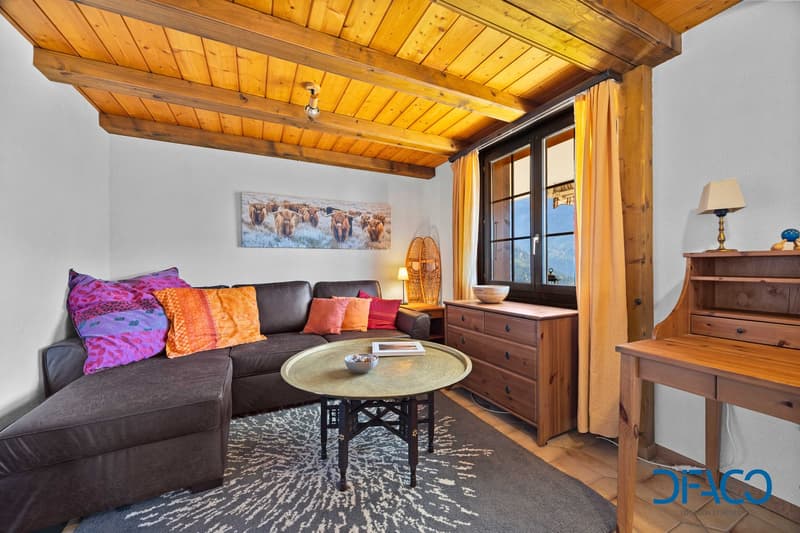 Leather couch, L-shaped, various pillows, large coffee table, decorative bowl, rug, wooden dresser, wooden desk, lamp, picture, wooden ceiling, white walls, window, curtains