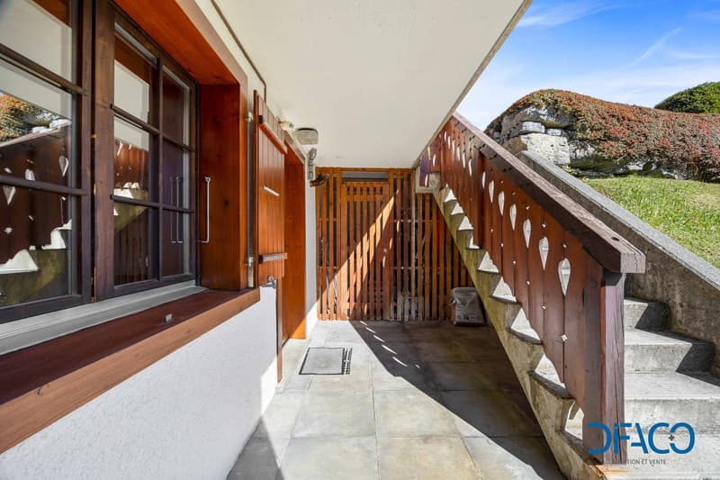 Raised ground floor building with wooden entrance doors and a wooden handrail on stairs