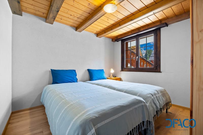 Double bedroom with two twin beds, blue bedding, wooden floor, wooden ceiling, lamp, window with alpine view