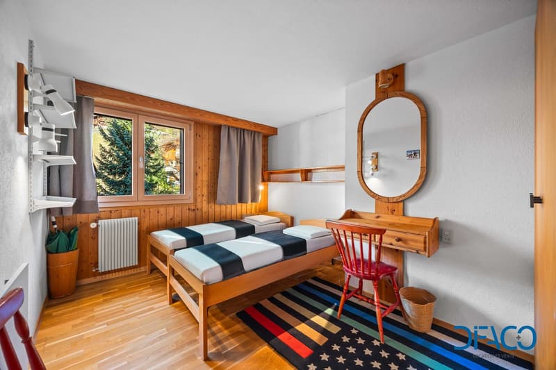 Two single beds, wooden desk, chair, mirror, radiator, windows, wooden floor