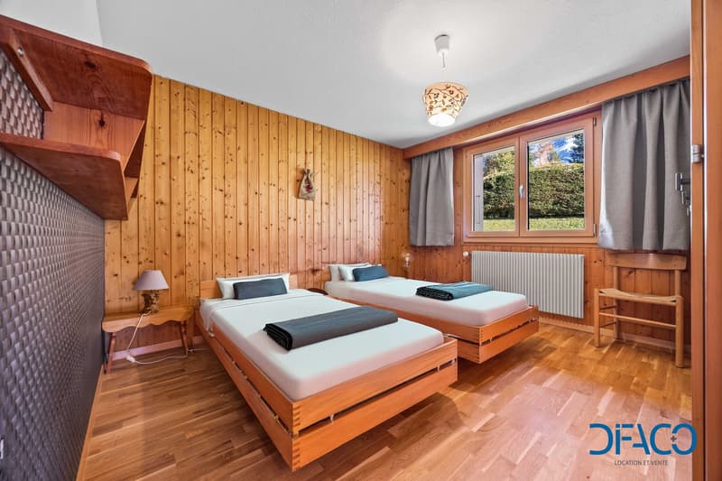 wooden walls, wooden bed with mattresses, bedside table with lamp, radiator, windows with curtains