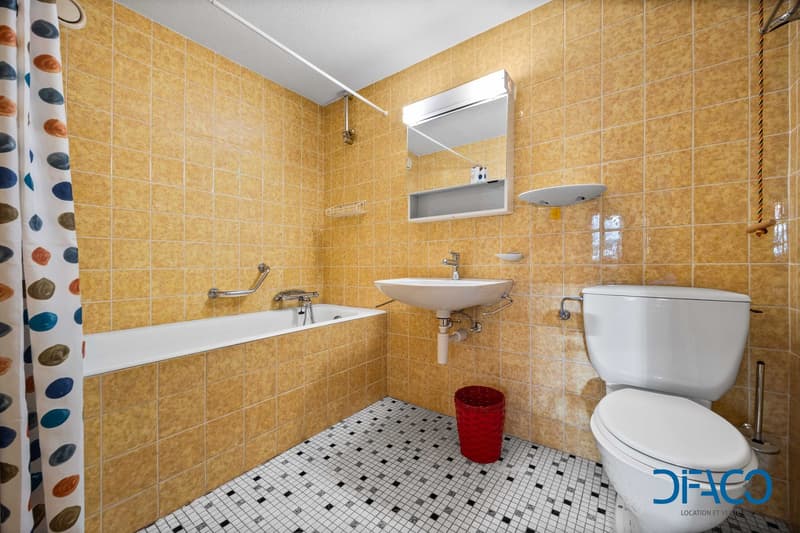 Bathroom: yellow tiles, white bathtub, white sink, white toilet, red basket, mirror