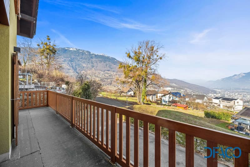 Wide balcony with wooden railing, panoramic mountain views, clear sky, greenery