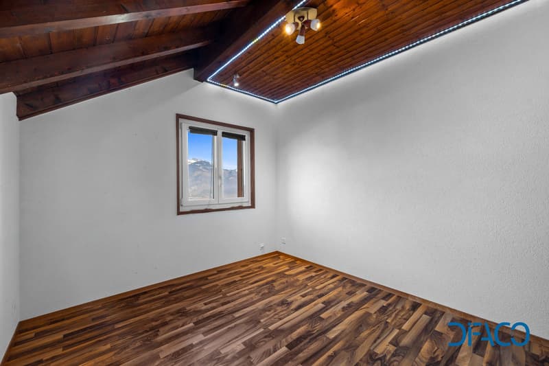 Empty room with wooden flooring, white walls, wooden ceiling, a window offering a view of mountains