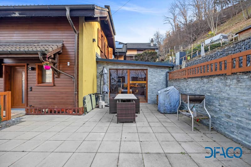 Timber exterior, brick wall, door, large terrace with table, and a covered area with a grill