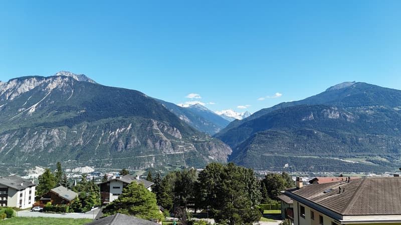 Aerial view of houses in a valley with mountainous backdrop under a clear blue sky