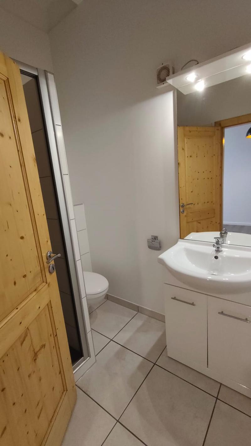 white tiles, white sink, white toilet, wooden door, mirror, wooden cabinet