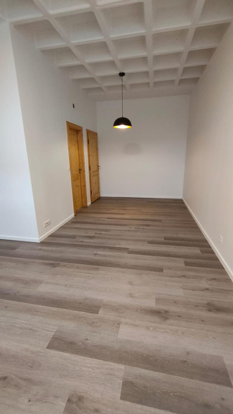 empty room, wooden floor, white walls, wooden doors, ceiling with square panels, light fixture