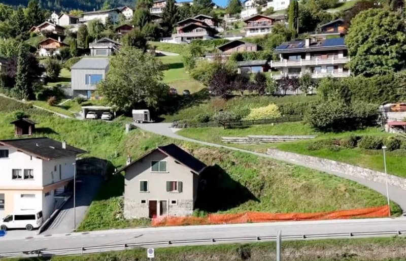 residential houses on slope, grassy hill, road with vans, trailer parked