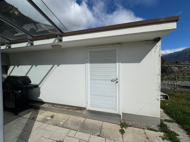white building with a glass roof, white door, black grill, tiled floor, security camera