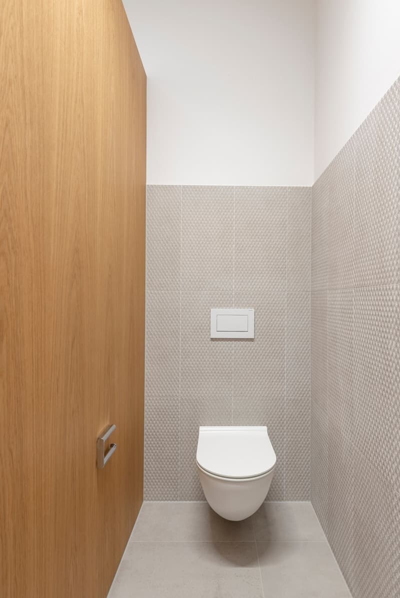 wooden door, wall mounted toilet, white tiles, silver fixtures