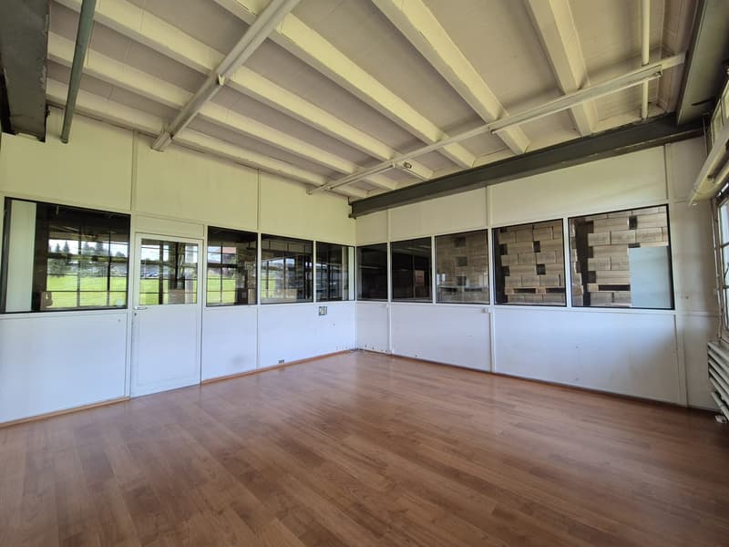 Empty room with hardwood floors, high ceilings, large windows facing outdoors, recessed lighting.