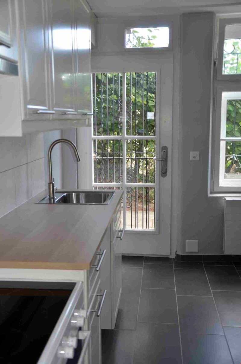 modern kitchen with white cabinets, stainless steel sink, faucet, tiled floor, glass door with metal grill, window with view to outside