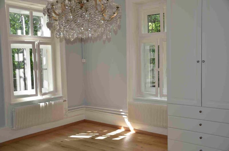 Chandelier, white walls, large windows, white wooden floor, white radiators, white wardrobe