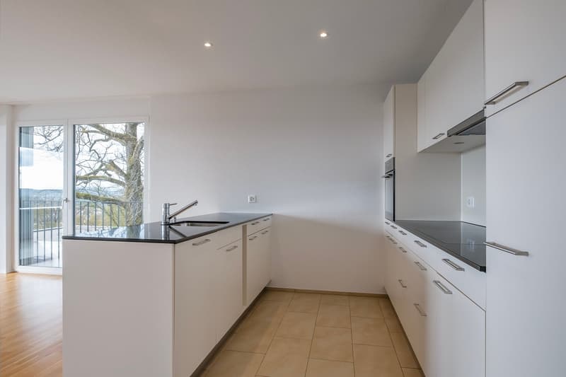 modern kitchen, white cabinets, black countertops, stainless steel sink, faucet, sliding glass door to balcony, tiled floor, white walls, ceiling lights