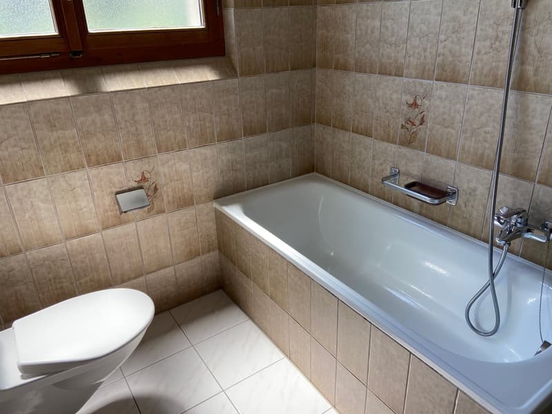 Bathroom with white tiles, bathtub, toilet, and shower head