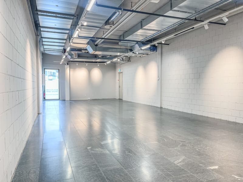 Empty room with white walls, gray floor, ceiling lights, and an open door.
