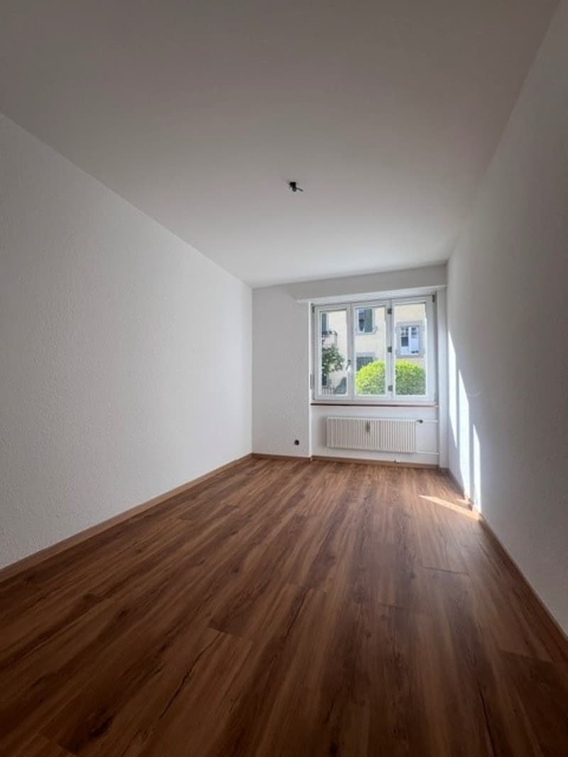 empty room, wooden floor, white walls, large window, white radiator
