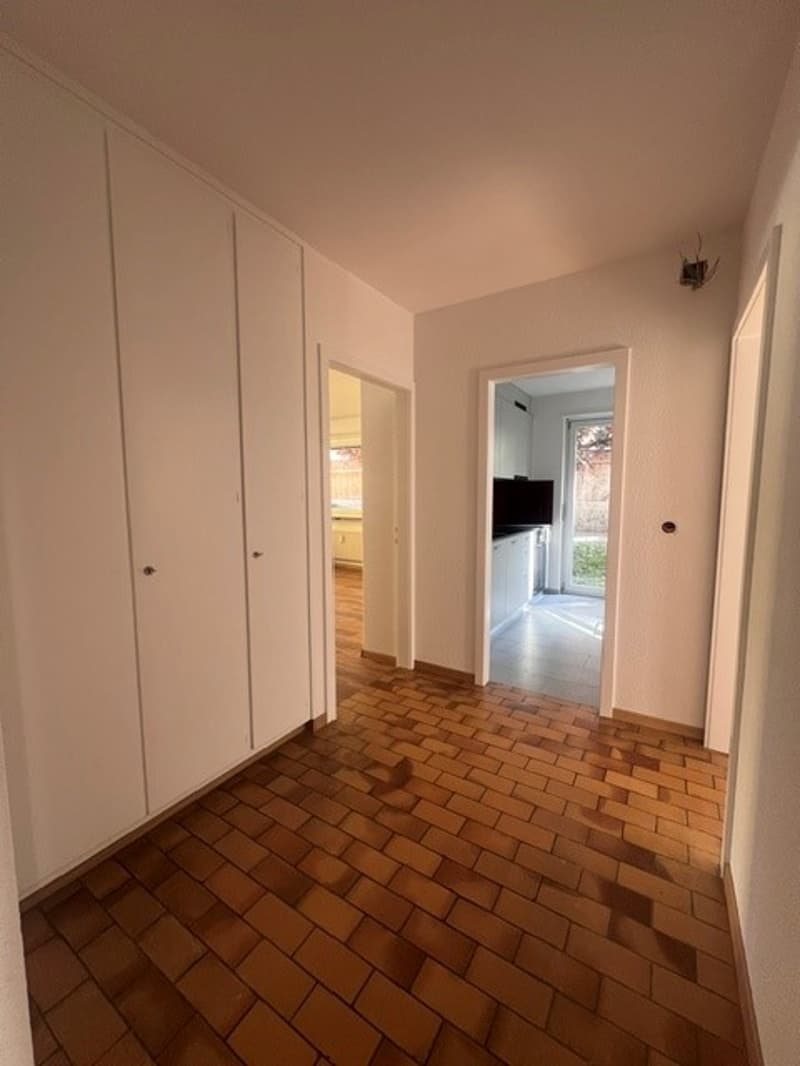 Empty room with wooden floor, white walls, white cabinets, and two doors leading to other rooms
