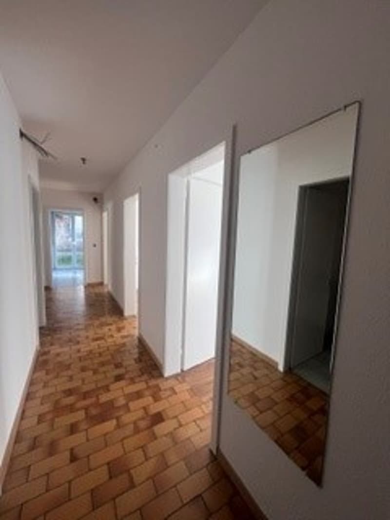 Empty hallway with wooden floor, white walls, mirror, doors