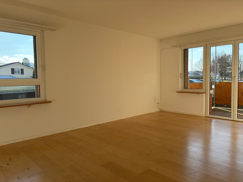 empty room, wooden floor, white walls, two windows, sliding glass doors to balcony, power outlet