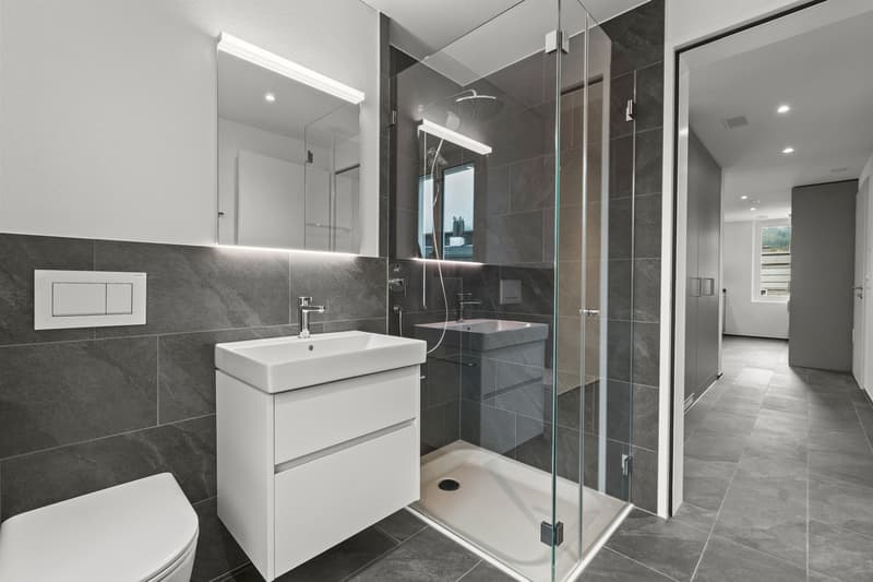 Tiled floor, Glass shower enclosure, White sink, White toilet, Built-in mirror with integrated lighting, Modern fixtures