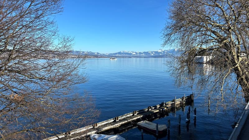 A view of a lake, mountains in the distance, a wooden dock, a small covered boat, clear skies