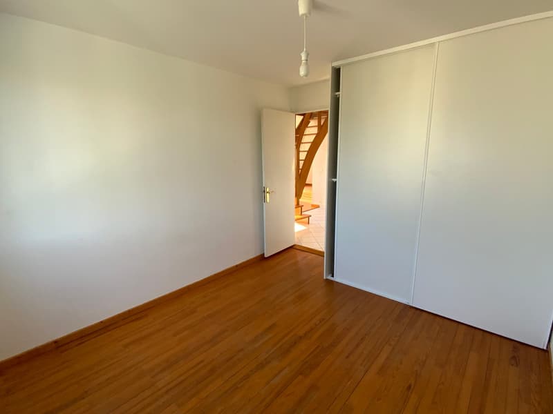 Empty room with wooden flooring, white walls, open door, wooden stairs visible