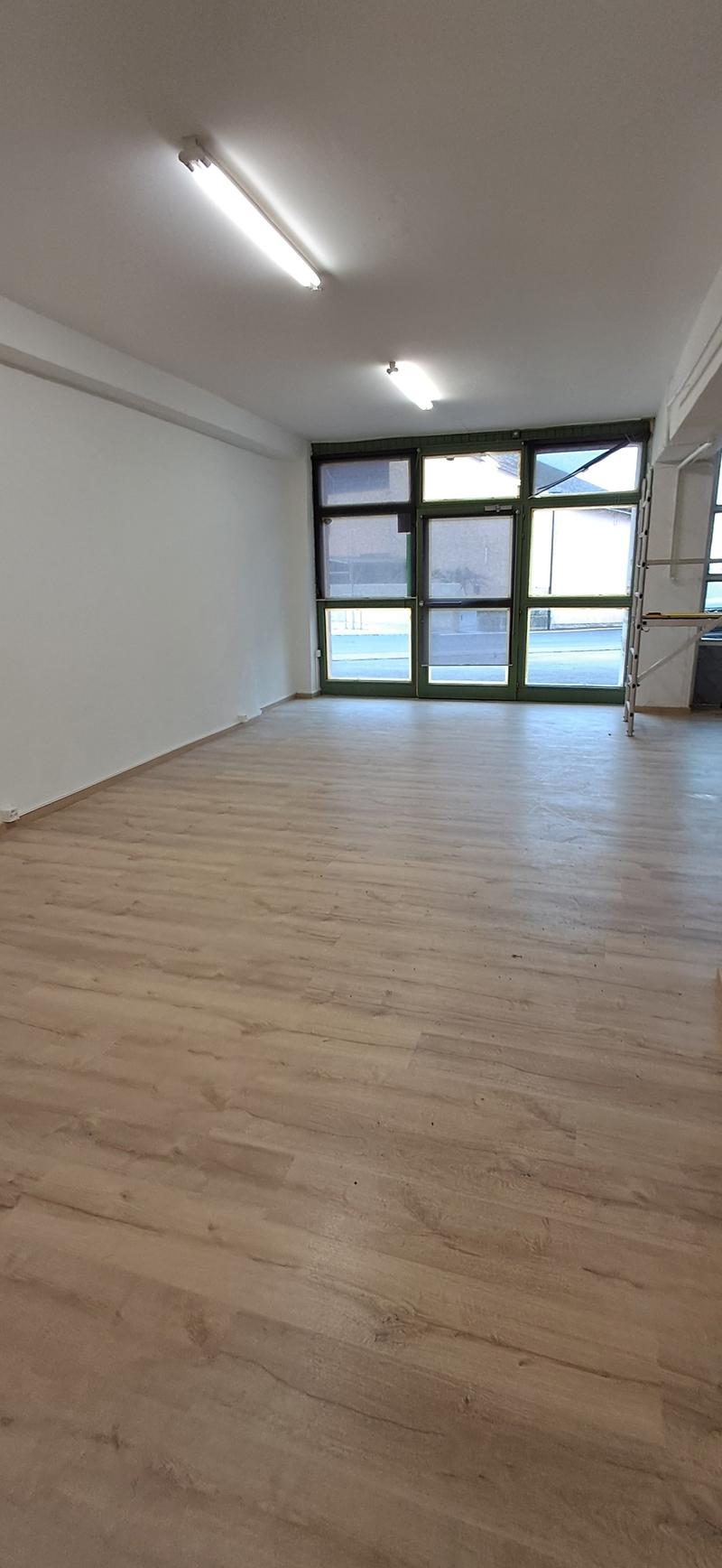 large empty room, wooden floor, fluorescent ceiling lights, large glass windows
