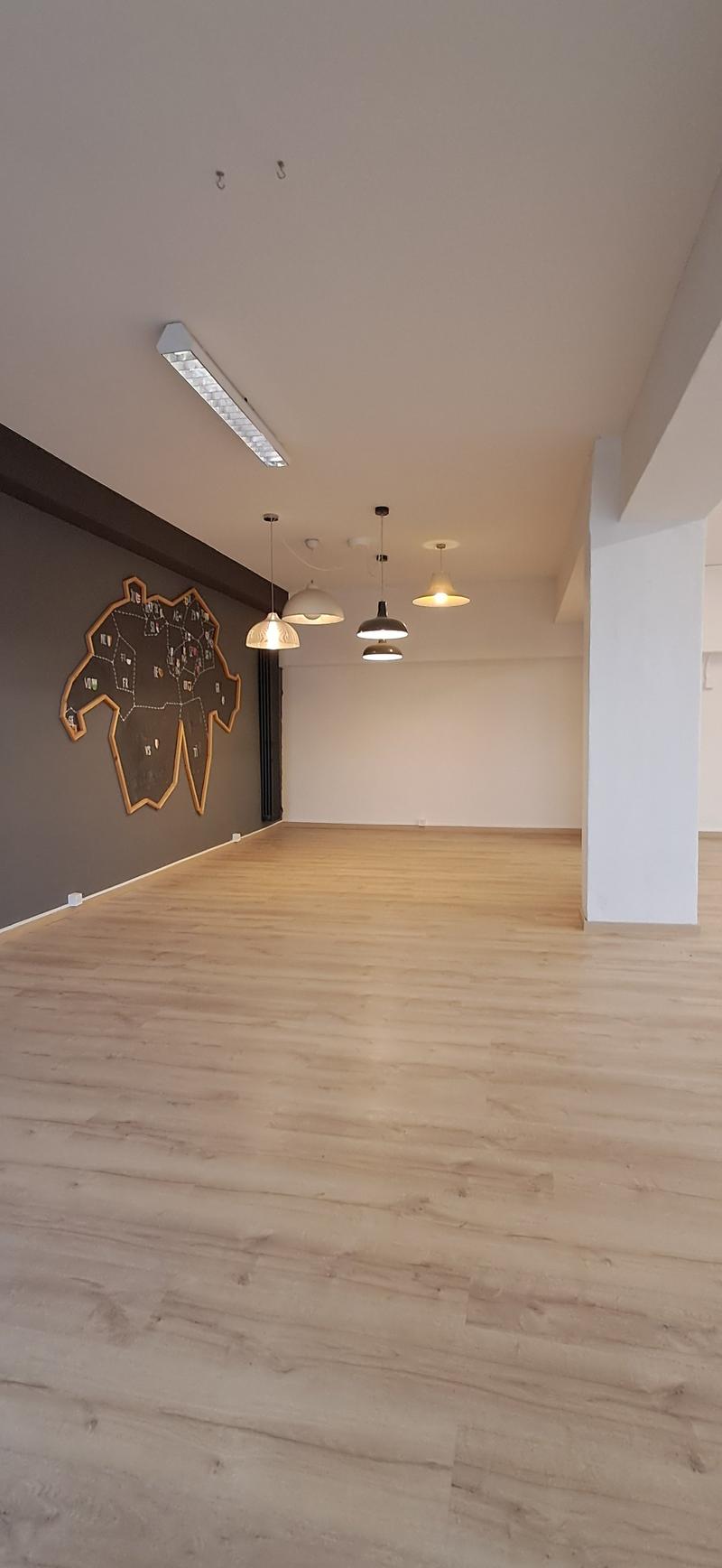 large empty room, hardwood floor, 5 hanging lamps, wooden art piece on wall