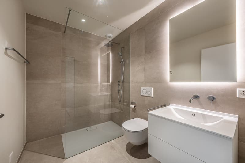 Modern bathroom with a glass shower enclosure, white fixtures, and beige tiles.