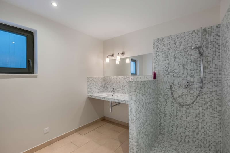White walls, white tiled flooring, a sink with a faucet, a mirror, and a shower with a showerhead.