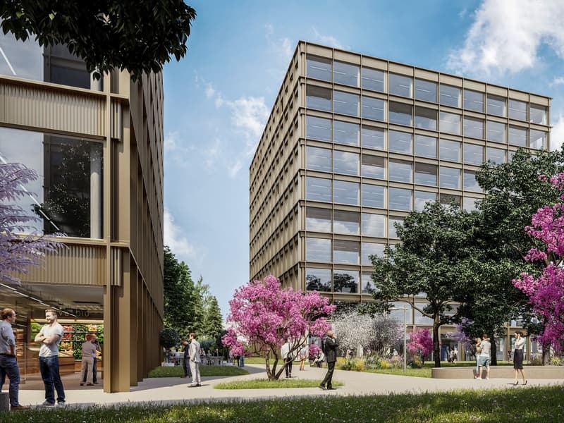 A modern multi-story commercial building with a glass and metal facade, surrounded by lush greenery and blooming trees. The building has balconies or terraces visible, and the overall scene suggests a pleasant outdoor environment with people walking aroun