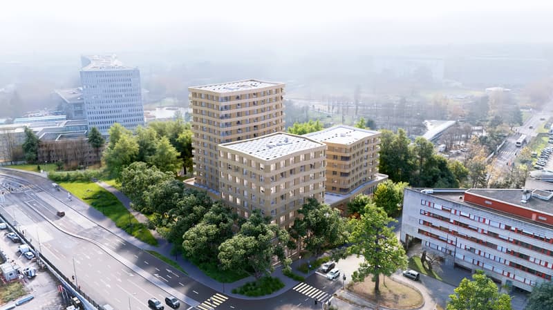 Aerial view of a multi-story residential building with a modern, angular design. The building has several balconies and is surrounded by trees and other buildings in an urban setting.